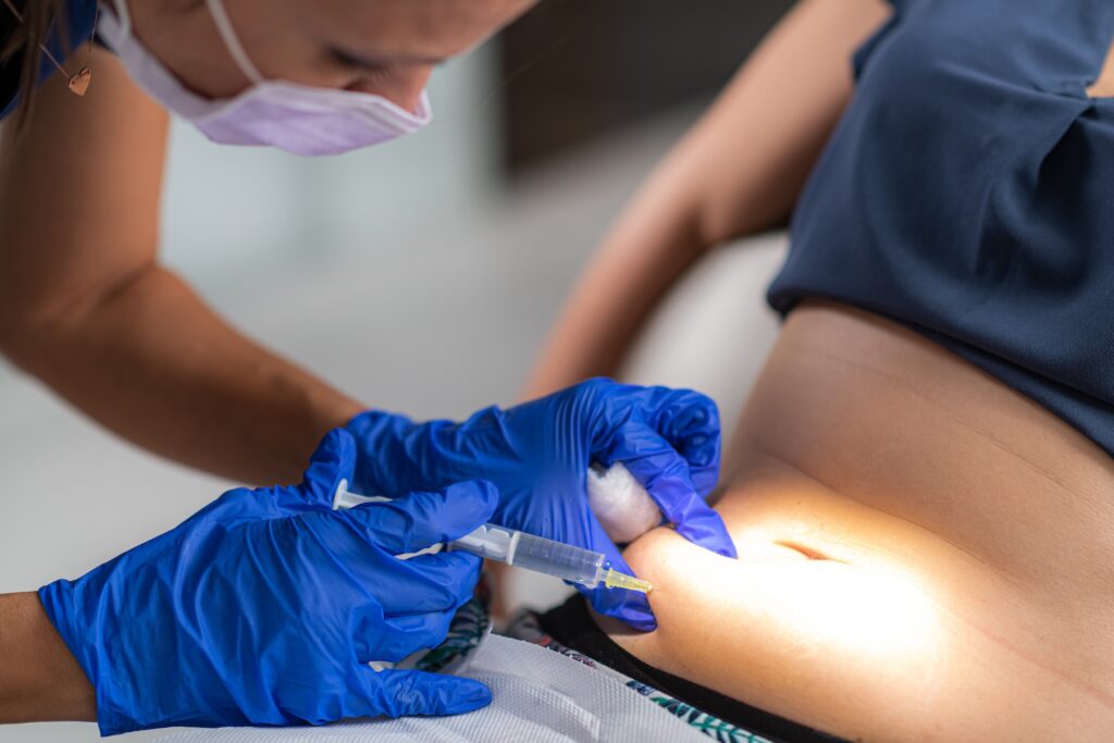 A provider at Total Skin administers a weight loss injection, wearing medical gloves as they place the shot in the patient's abdomen. These types of medication can often accelerate weight loss in Fargo.