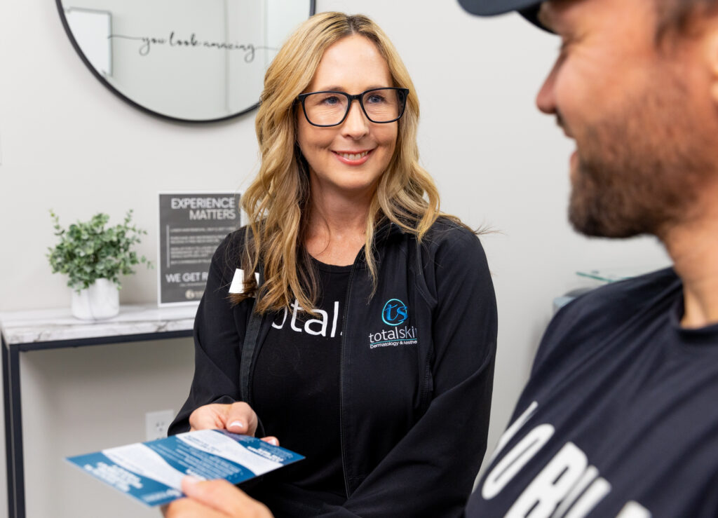 A provider at Total Skin hands a pamphlet on TRT in Grand Forks to a patient, both of them smiling. This pamphlet covers the basics of the treatment and what you can expect.