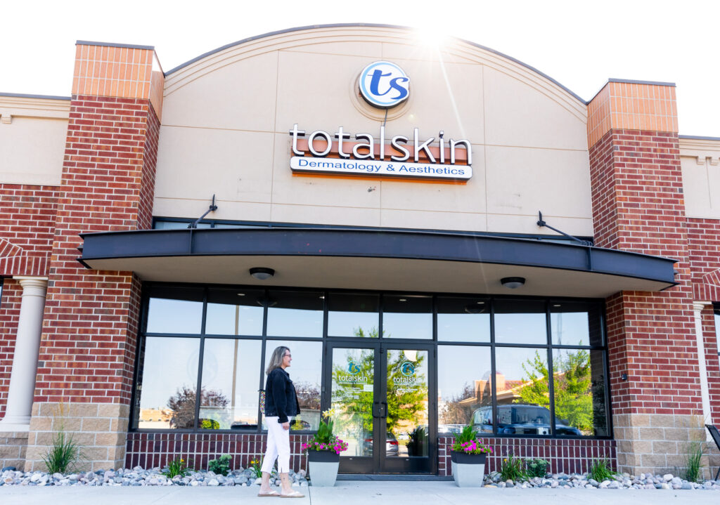 The front entrance of Total Skin, a wide shot of the front door, exterior sign, and main building. A patient is walking towards the front door for their Emsculp NEO near West Fargo appointment.